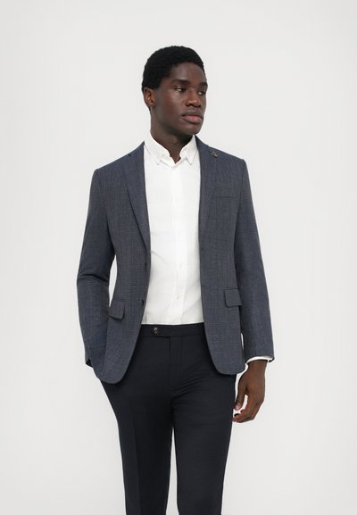Marinefarbener strukturierter Blazer mit zwei Fronttaschen, einem Knopf und einem weißen Hemd mit Kragen. Slim-Fit-Stil mit dunkler Hose.