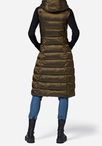 Długa oliwkowozielona kamizelka puchowa z kapturem, z poziomymi pikowanymi panelami, noszona na czarnej prążkowanej bluzce, zestawiona z niebieskimi dżinsami i czarnymi botkami.