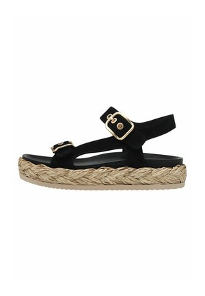 Sort sandal med to gyldne spænderem og flettet naturfiber plateau sål mod hvid baggrund.