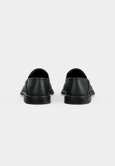 Ζευγάρι μαύρα δερμάτινα παπούτσια τύπου slip-on, εμφανιζόμενα από πίσω σε ένα απλό ανοιχτό γκρι φόντο.