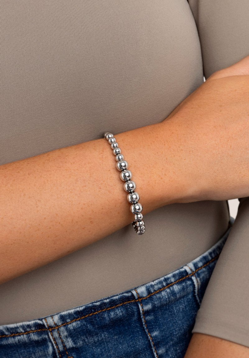 Bracelet en perles d'argent avec des perles sphériques polies de tailles variées, passant en douceur du petit au grand, sur un teint de peau clair.