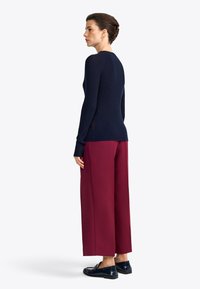 Marineblauwe geribde trui met lange mouwen, gecombineerd met brede bordeauxrode broeken en donkere loafers. Het ontwerp heeft een textuur stof en strakke lijnen.
