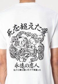Hvid bomulds-t-shirt med et grafisk tryk på ryggen, der viser to kranier snoet med slanger, detaljeret i sort blæk, sammen med japansk tekst.