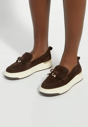 Brown suede shoes with a rounded toe, decorative laces, and a white midsole. Features a metallic accent on the heel and textured rubber sole.