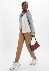 Lichtblauwe gebreide trui, crème- en bordeauxrode sjaal, beige leren broek, witte sneakers met accenten, en een bordeauxrode handtas met logo.