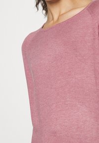 Vaaleanpunainen pitkähihaisen neulepaita, ribbineulosta, pyöreä kaula-aukko, vartalonmyötäinen malli, hienovaraisilla saumatiet yksityiskohdilla ja pehmeä, hengittävä kangas.