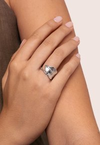 Silberner Ring mit einem Blattform-Design, das eine detaillierte Textur und ein glattes Band aufweist, getragen an einer Hand mit heller Nagellack.