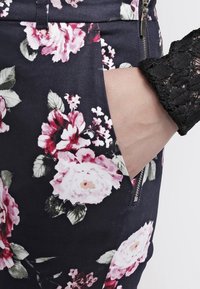 Květinová sukně s tmavým pozadím, růžovými a bílými růžemi, boční kapsou a zipovým detailem, vyrobená z hladkého materiálu.