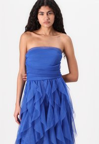 Royal blue strapless dress made of layered tulle. Features a fitted bodice and a ruffled skirt with varying lengths. Smooth texture throughout.