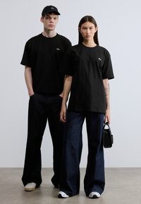 Μαύρα βαμβακερά μπλουζάκια με κοντά μανίκια, συνδυασμένα με σκούρα μπλε τζιν με φαρδιά πόδια. Τα αξεσουάρ περιλαμβάνουν μαύρο καπέλο και μικρή τσάντα.