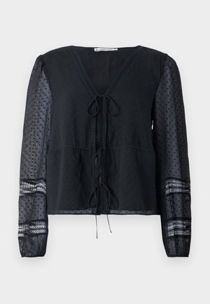 Sort semi-transparent bluse med lange prikkede ærmer, blondekant, V-hals med to bundet sløjfer ned ad forsiden.