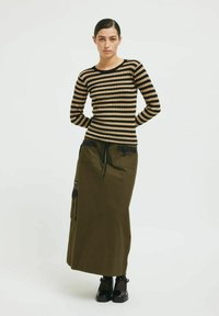 Top de punto de manga larga a rayas en beige y negro, combinado con una falda de cintura alta en verde oliva que cuenta con bolsillos tipo cargo y cordón.