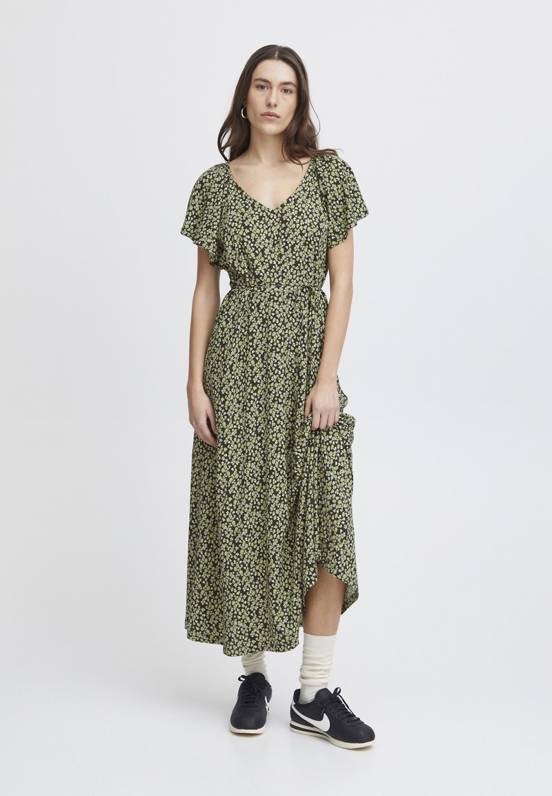 Floral print dress in dark green with a v-neck, short flutter sleeves, and a tie waist, paired with black sneakers and cream socks.