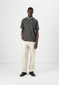 T-shirt en coton gris, coupe décontractée, assortie à un pantalon large crème. Des chaussures noires et une écharpe rayée mettent en valeur la tenue.