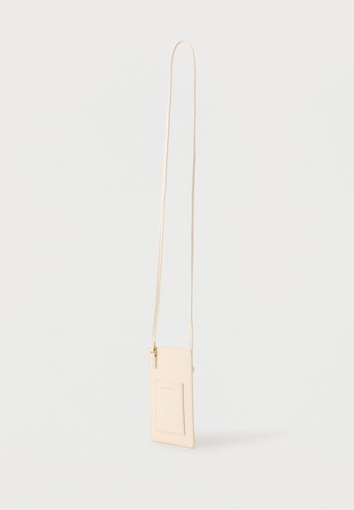 Μπεζ δερμάτινο θήκη τηλεφώνου χιαστί με μπροστινή θήκη για κάρτες και μακρύ λεπτό ιμάντα, εμφανίζεται κρεμασμένο σε λευκό φόντο.