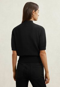 Črn pleten pulover s kratkimi rokavi z rebrastim ovratnikom in robom, z oprijeto zasnovo in mehko teksturo, nošen s črnimi kavbojkami iz jeansa.