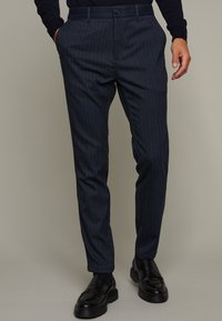 Pantalon slim rayé marine en tissu texturé ; coupe ajustée avec poches latérales ; associé à des mocassins noirs élégants.