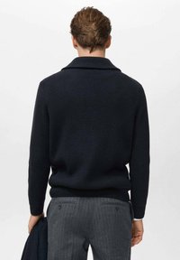 Maglione knit blu scuro con colletto a scialle, finitura testurizzata e stile aderente, abbinato a pantaloni grigi a righe sottili.