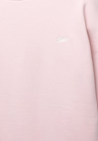 Hellrosa Sweatshirt mit kleinem weißen gesticktem "Santz"-Logo auf der linken Brust und sichtbarer Naht am rechten Ärmel.