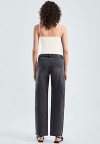 Schwarze weit geschnittene Jeans mit hoher Taille und zwei Gesäßtaschen, kombiniert mit einem leichten Tanktop. Gerades Bein und minimale Details.
