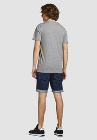 Graues Kurzarm-T-Shirt kombiniert mit hochgerollten dunklen Jeansshorts und schwarzen Sneakers. Die Rückansicht zeigt einen lässigen Schnitt und entspannten Stil.
