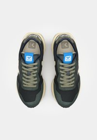 Green and navy sneaker with a black upper, beige sole, and grey accents. Features flat laces and a blue logo on the tongue.