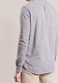 Szara koszula z długim rękawem, z kołnierzykiem na guziki, miękka w dotyku i z zaokrąglonym dołem. Posiada zapięcia na guziki na mankietach.