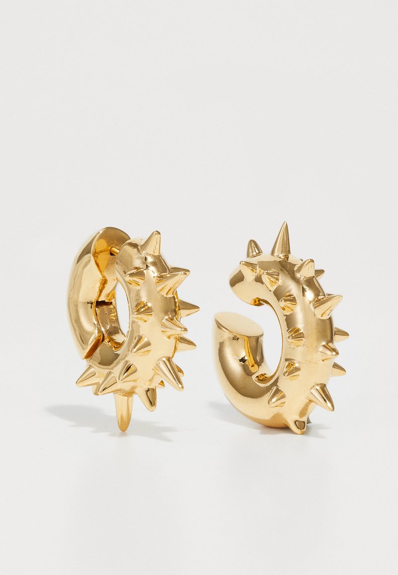 Cercei din aur cu un design în formă de vârfuri. Textura este netedă, cu ornamente punctate proeminente, distribuite uniform pe întreaga suprafață.