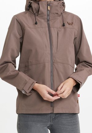 Person trägt eine mauvefarbene Kapuzenjacke mit Frontreißverschluss und Kordelzug, passt die Ärmelbündchen an, kombiniert mit grauen Jeans.