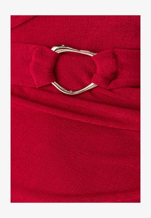 Czerwona sukienka z tkaniny z fakturowaną powierzchnią, ozdobiona kokardą i metaliczną klamrą w kształcie serca na talii.