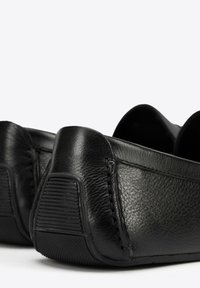Mocasines de cuero negro con un acabado texturizado, que cuentan con suelas de goma flexibles y costuras visibles a lo largo de los bordes.