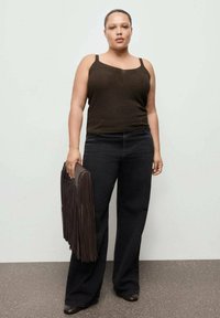 Top maro metalizat asortat cu blugi largi de culoare închisă. Ținând o geantă maro cu franjuri. Design minimalist cu o textură netedă.