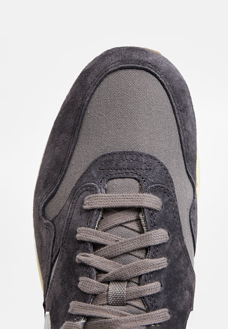 Grijze sneaker met een combinatie van gladde suede en textiel. Rondte neus, platte veters en een rubberen zool met een lichte accentkleur.