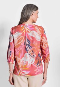 Blusa floreale in tonalità di rosa, arancio e bianco; tessuto leggero con maniche a tre quarti e polsini elasticizzati; presenta audaci motivi di foglie.
