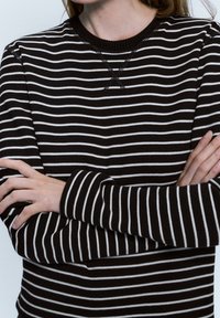 Maglione a strisce bianche e nere con scollatura rotonda, maniche lunghe e dettagli di cucitura sullo scollo. Texture morbida.
