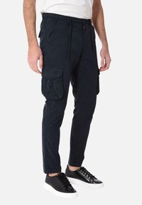 Pantaloni cargo blu navy in cotone con vestibilità slim, dotati di tasche laterali e una tasca cargo. Indossati con sneakers nere.