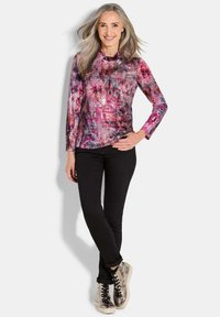 Kleurige lange mouw top met een roze en paarse abstracte print, gecombineerd met zwarte slim-fit broek en zilveren high-top sneakers.