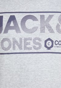 T-shirt in cotone grigio con un audace design testuale in viola scuro che recita "JACK & JONES". Include un dettaglio decorativo a logo esagonale.
