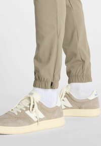 Zapatillas beige con acentos blancos y cordones crema. Parte superior de ante texturizado. Puños de pantalón de elastano beige claro, con detalle de cremallera en el dobladillo.