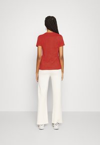 Camiseta roja de manga corta con cuello redondo, combinada con pantalones de pierna ancha de color claro y zapatillas blancas. Diseño simple, sin patrones visibles.