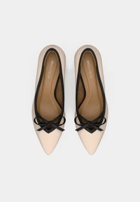 Pár béžových baletiek s špicatou špičkou, čiernym lemovaním a mašľou, zobrazených zhora na bielom pozadí.
