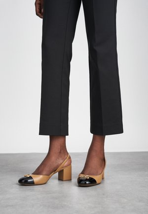 Slingback heeled shoes with a beige leather upper, black patent toe cap, and block heel. Gold accent detail on the toe adds elegance.