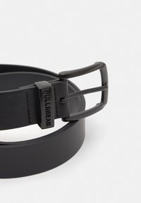 Zwarte leren riem met een matte zwarte rechthoekige gesp met reliëflogo. Soepele textuur en klassiek ontwerp.