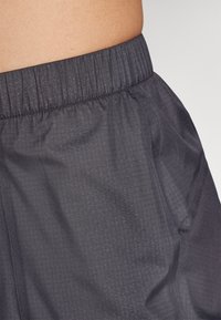 Dark gray athletic shorts with a textured fabric, featuring an elastic waistband and side pockets. Close-up view highlights the material.