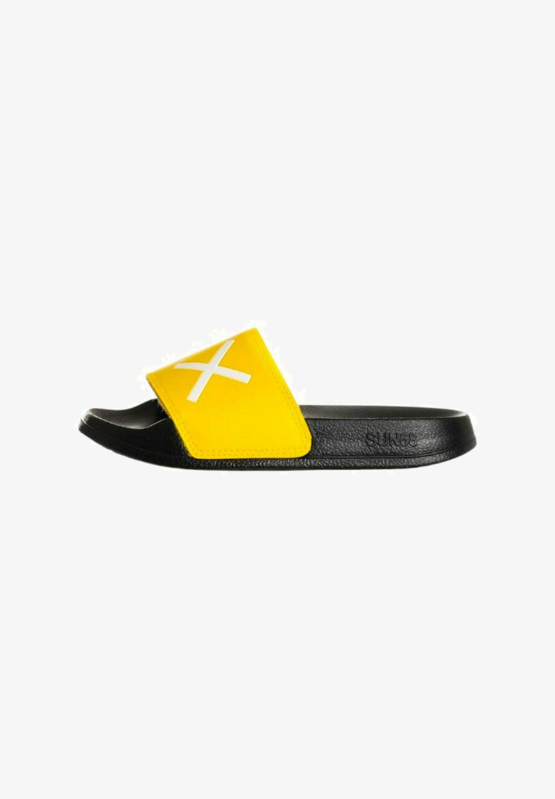 Sandalia deslizante negra y amarilla con una amplia correa amarilla que presenta una "X" blanca. Suela negra texturizada, diseño minimalista.