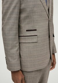 Brauner karierter Anzug aus strukturiertem Stoff. Verfügt über einen Zwei-Knopf-Verschluss, einen Slim-Fit-Schnitt und kontrastierende dunkelbraune Taschenakzente.