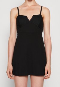 Robe noire avec bretelles ajustables, décolleté en V, corsage texturé et jupe lisse. Caractéristiques des accents en dentelle sur les bretelles et le décolleté.