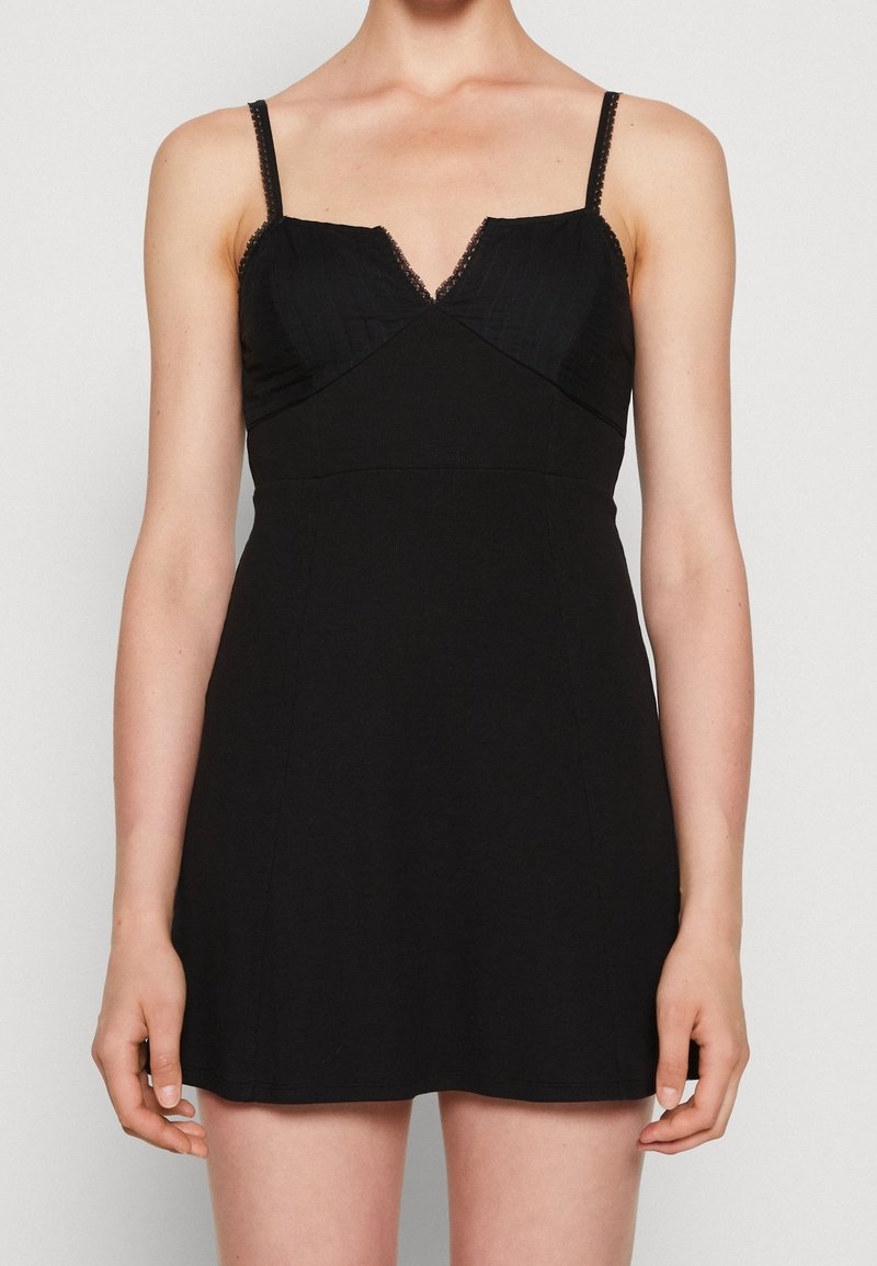 Robe noire avec bretelles ajustables, décolleté en V, corsage texturé et jupe lisse. Caractéristiques des accents en dentelle sur les bretelles et le décolleté.