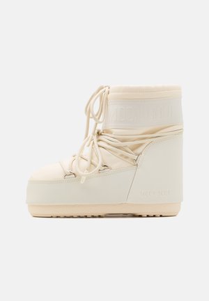 Cream-colored Moon Boot with a padded shaft, lace-up front, and textured rubber sole. Features a logo on the upper and a chunky shape.