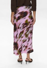 Gonna maxi in tessuto leggero e liscio con sfondo rosa e motivi astratti in verde scuro e marrone. L'orlo termina con una leggera curvatura.